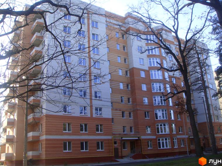 Фасад житлового комплексу Столиця Околиці з цегляним оздобленням та балконами. Навколо будівлі дерева та зелена зона.