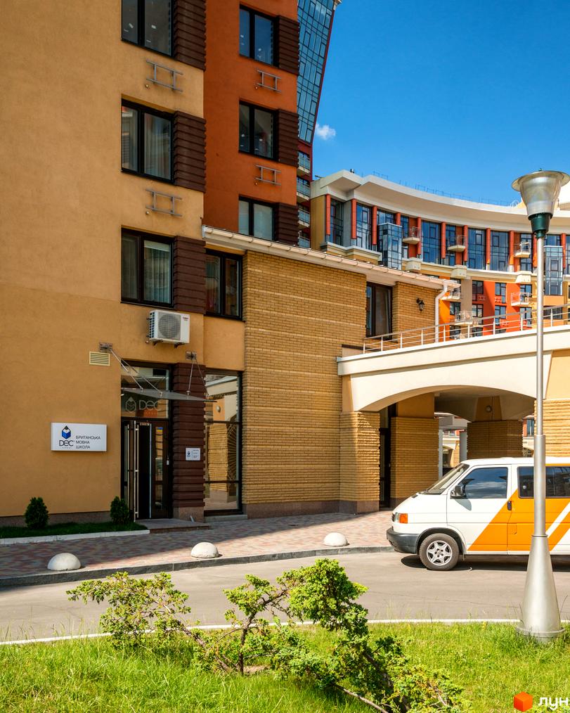 Житловий комплекс Сонячна брама з бежево-помаранчевим фасадом, вікнами та скляними елементами. Навколо зелений газон, дорога.