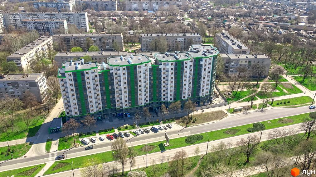 Житловий комплекс Comfort City: багатоповерховий будинок з біло-зеленим фасадом. Вид зверху на комплекс біля дороги та зелених зон.
