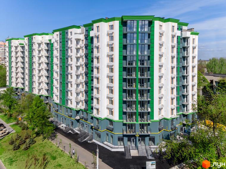 Житловий комплекс Comfort City з біло-зеленим фасадом та балконами, оточений зеленими насадженнями та доріжками.