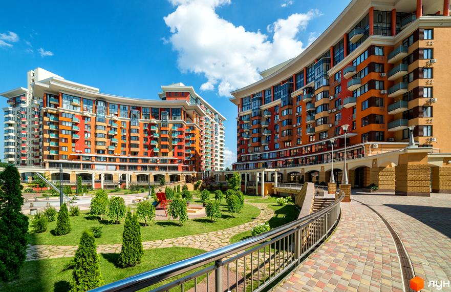 Житловий комплекс Сонячна брама: два багатоповерхові будинки з вигнутими фасадами та кольоровими балконами. На території є зелені насадження та дитячий майданчик.