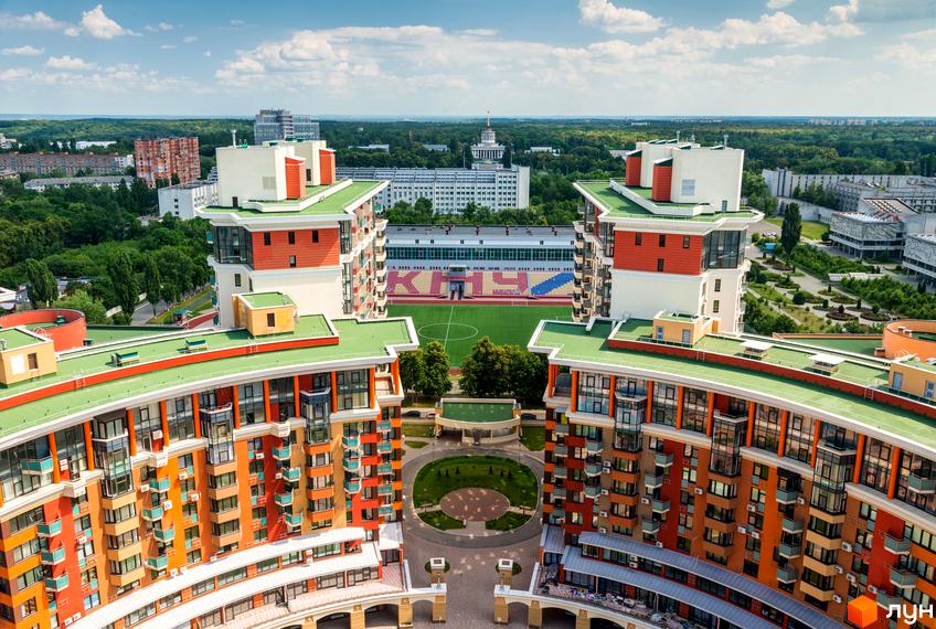 Комплекс Сонячна брама: вигнуті будинки з різнокольоровими фасадами та зеленими дахами. Внутрішній двір з газоном, поруч стадіон та забудова.