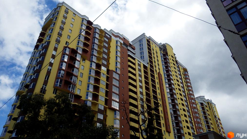 Житловий комплекс на вул. Коперника, 7: багатоповерховий будинок з жовто-коричневим фасадом, великими вікнами та балконами, оточений деревами.