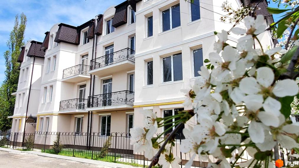 Зображення фасаду будинку Житловий комплекс вул. Академіка Вернадського (Тульська), 21а, з балконами та кованими огорожами, на фоні блакитного неба та квітучих дерев.