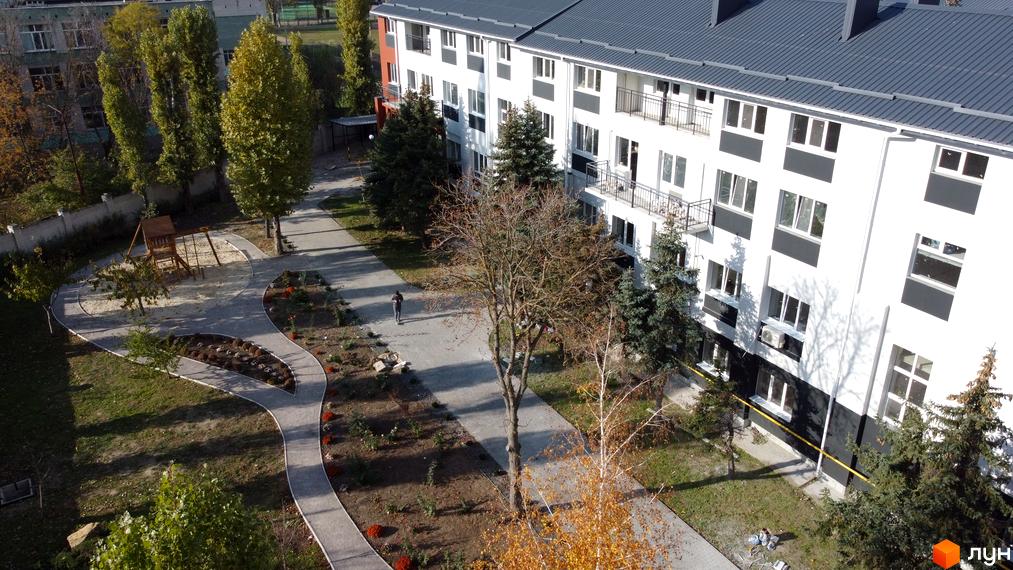 Житловий комплекс Park Stone: біло-чорна будівля з балконами та вікнами, зелена прибудинкова територія з дитячим майданчиком та деревами.