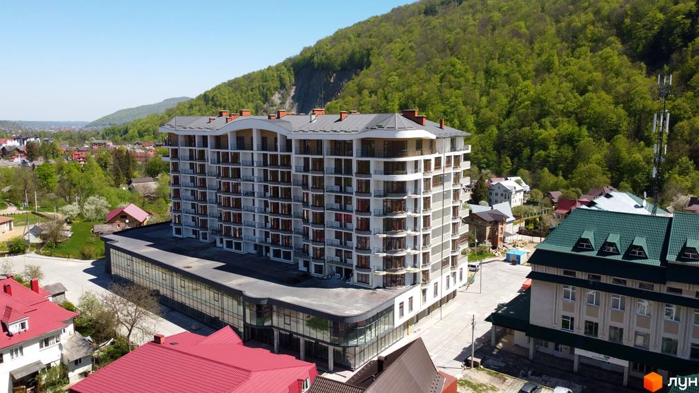 Житловий комплекс Скеля - багатоповерховий будинок з балконами та панорамними вікнами, розташований серед зелених пагорбів та інших будівель.