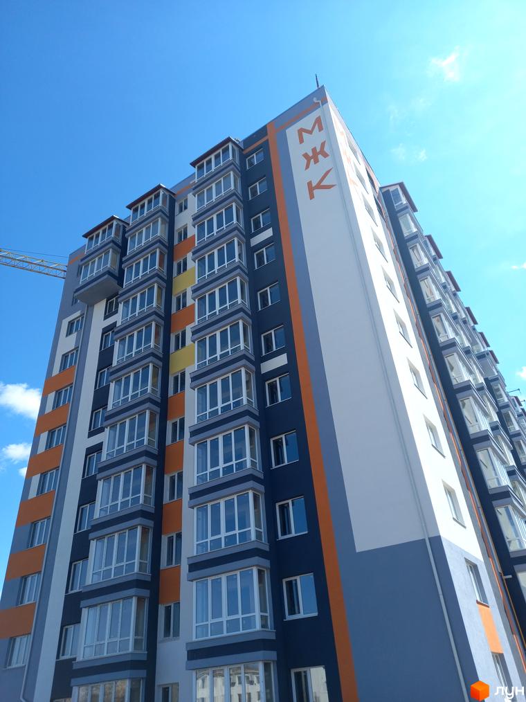 Багатоповерховий будинок Житлового комплексу Сім'я з синіми, сірими та помаранчевими фасадами, великими вікнами та балконами.