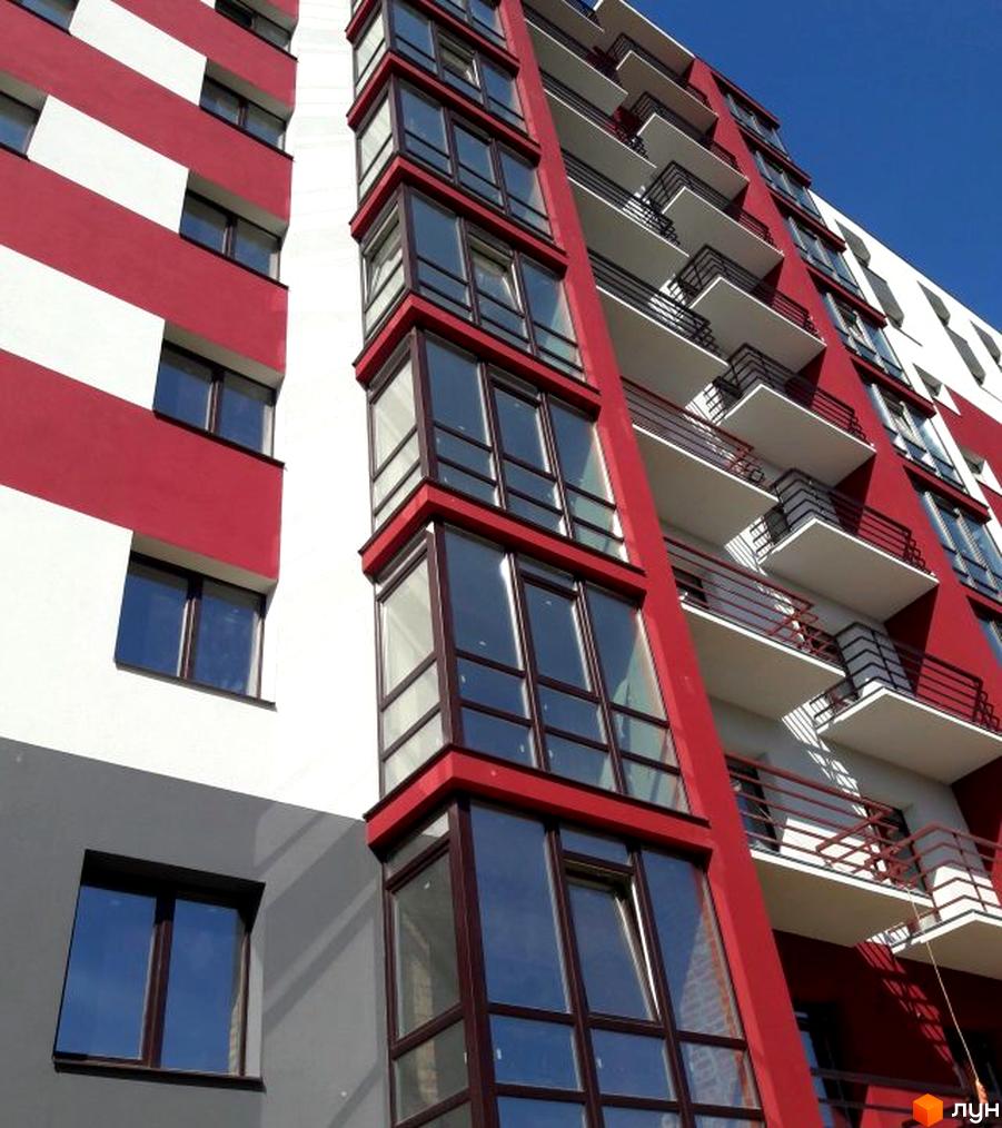 Фасад Житлового комплексу Центральний з червоно-білими смугами, заскленими лоджіями та балконами. Зображення будівлі на тлі блакитного неба.