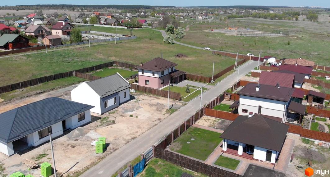 Котеджне містечко Михайлівський хутір: одно- та двоповерхові будинки з коричневими та сірими дахами, огороджені дерев'яними парканами. Навколо зелені газони та дорога.