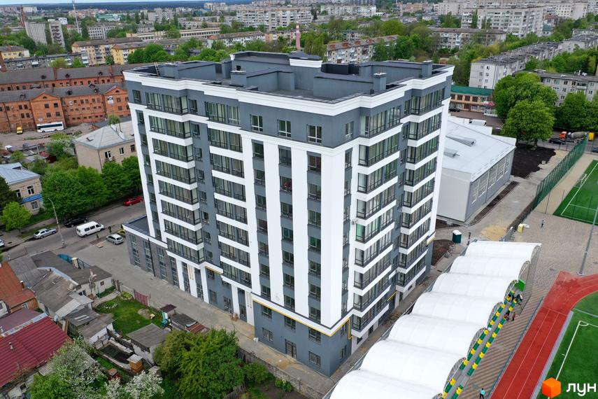 Новобудова Олімп, багатоповерховий будинок у сіро-білих тонах з великими вікнами. Поруч розташований спортивний комплекс з футбольним полем та біговою доріжкою.