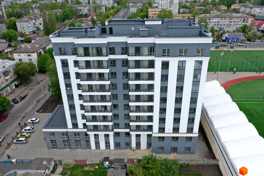 Житловий комплекс Олімп з біло-сірим фасадом та великими вікнами. Поруч розташовані дорога та спортивний стадіон.