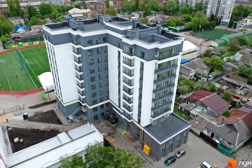 Новобудова Олімп, багатоповерховий будинок у біло-сірих тонах з великими вікнами. Поруч облаштовується прибудинкова територія та спортивне поле.