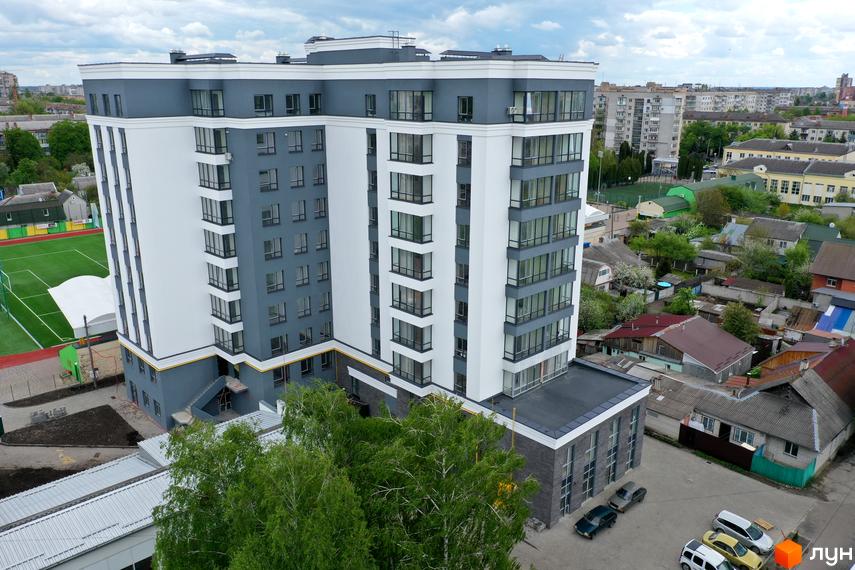 Новобудова Олімп: високий будинок з біло-сірим фасадом та великими вікнами. Поруч спортивний майданчик та міська забудова.