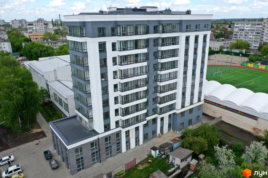 Багатоповерховий житловий будинок Житловий комплекс Олімп з сіро-білим фасадом та великими вікнами. Поруч розташовані спортивне поле та інші будівлі.