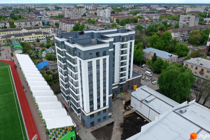 Житловий комплекс Олімп: багатоповерховий будинок біло-сірого кольору з великими вікнами, розташований поруч зі стадіоном.