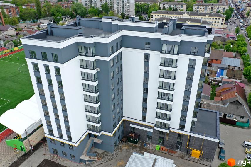 Житловий комплекс Олімп: багатоповерховий будинок з біло-сірим фасадом та великими вікнами, поруч зі спортивним полем.
