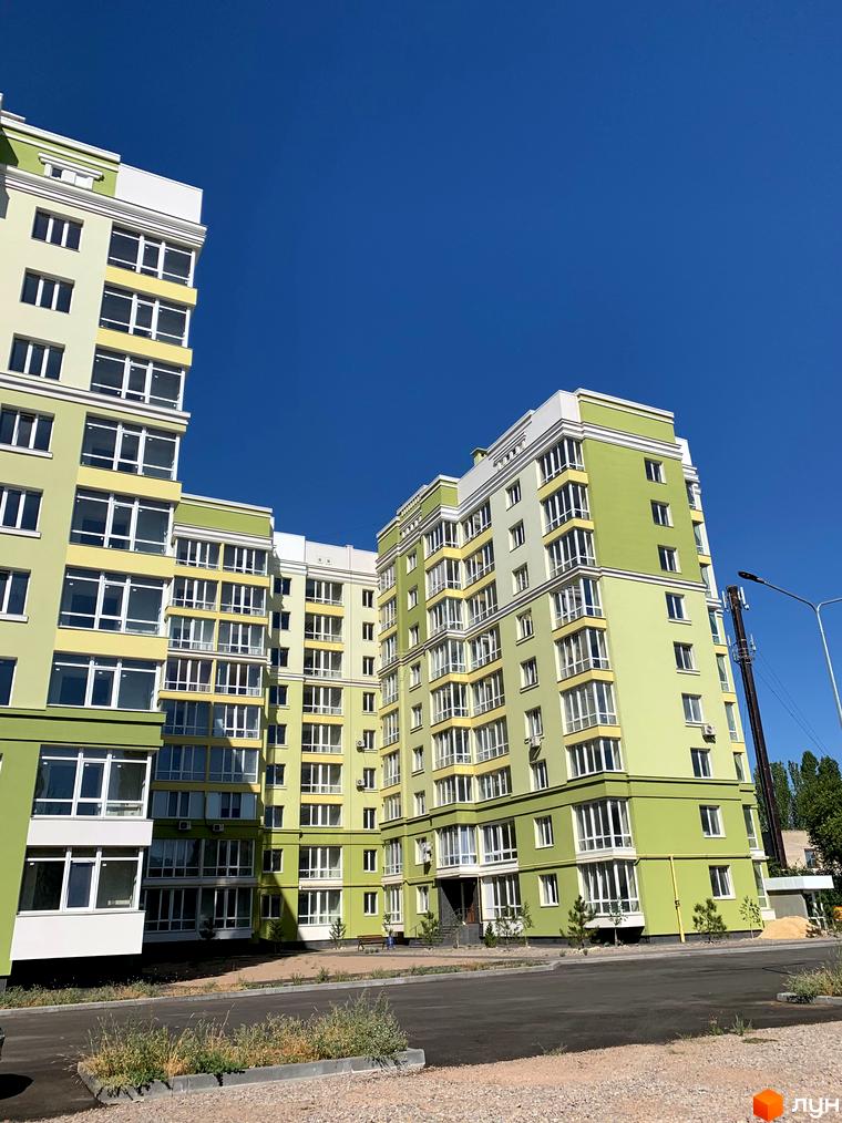 Житловий комплекс Levanevsky: багатоповерхові будинки світло-зеленого та жовтого кольору з білими вікнами та балконами. Прибудинкова територія має дорогу та молоді дерева.