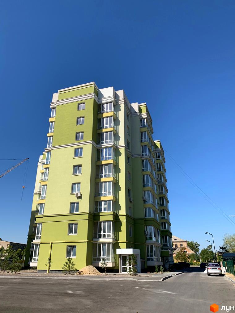 Зображення багатоповерхового будинку Житлового комплексу Levanevsky з великими вікнами та зеленим фасадом. На передньому плані асфальтована дорога та прибудинкова територія.