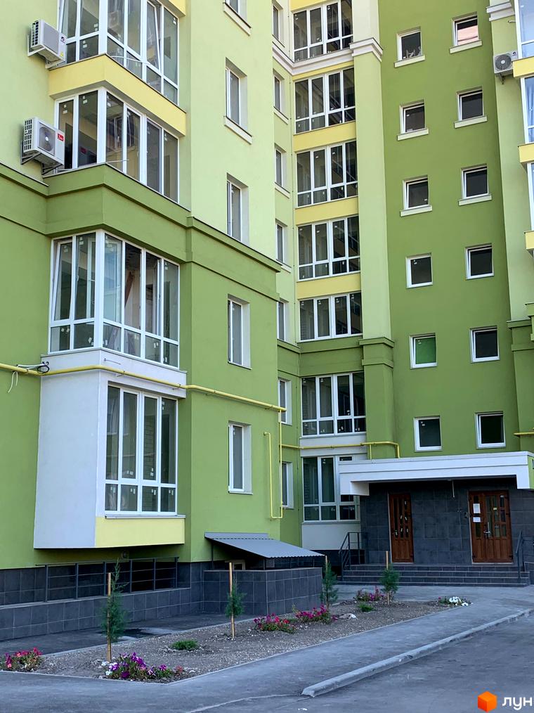 Зовнішній вигляд Житлового комплексу Levanevsky: зелений фасад з жовтими акцентами та великими вікнами. Прибудинкова територія з доріжками, молодими деревами та квітами.
