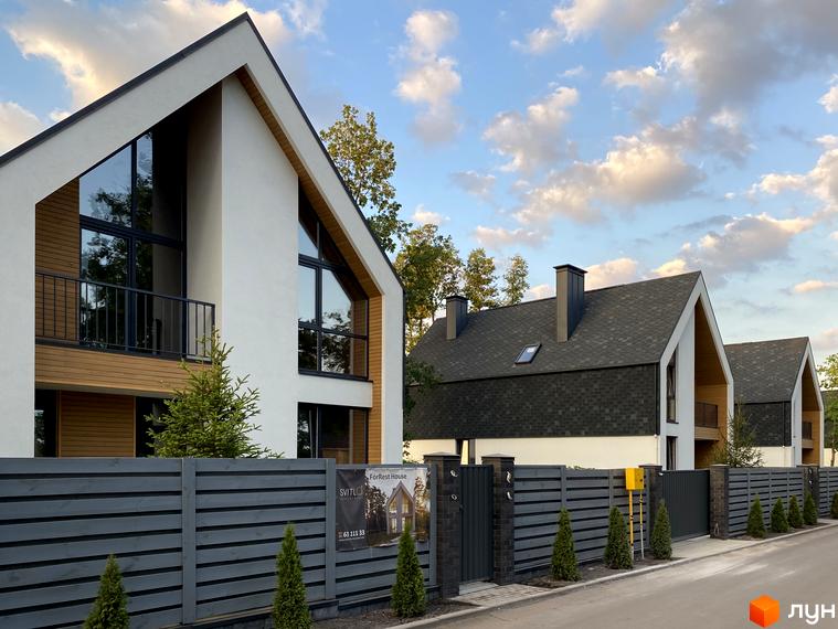 Котеджне містечко КМ Loft City: фасади будинків з великими вікнами та дерев'яними елементами, огороджена територія з туями та парканом.