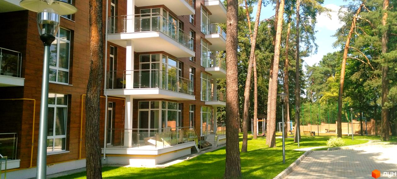 Житловий комплекс Грінвуд: багатоповерховий будинок з дерев'яним фасадом та скляними балконами. Навколо будинку зелена галявина, дерева та пішохідна доріжка.