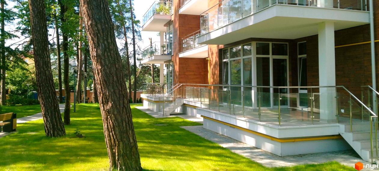 Житловий комплекс Грінвуд з дерев'яним фасадом та скляними балконами, оточений зеленим парком з деревами та газонами.