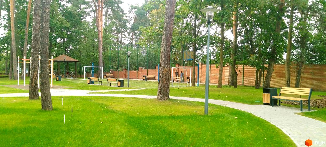 Житловий комплекс Грінвуд. Спортивний майданчик з футбольними воротами, баскетбольним щитом, брусами та лавками на тлі цегляної стіни та дерев.