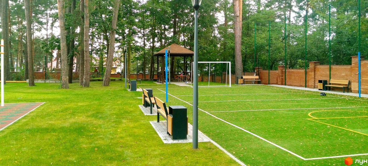 Житловий комплекс Грінвуд: зелена зона відпочинку зі спортивним майданчиком та місцями для сидіння. Комплекс оточений деревами, створюючи затишну атмосферу.