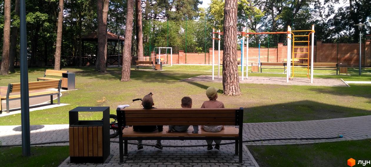 Житловий комплекс Грінвуд. Дитячий майданчик та зона відпочинку з лавками та урнами на фоні цегляної стіни та спортивного комплексу.