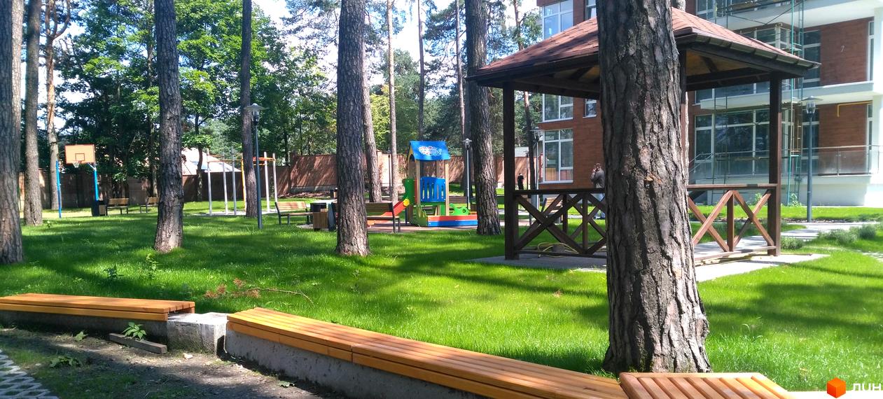 Житловий комплекс Грінвуд: цегляний будинок з великими вікнами та зеленою прибудинковою територією з дитячим майданчиком та місцями для відпочинку.