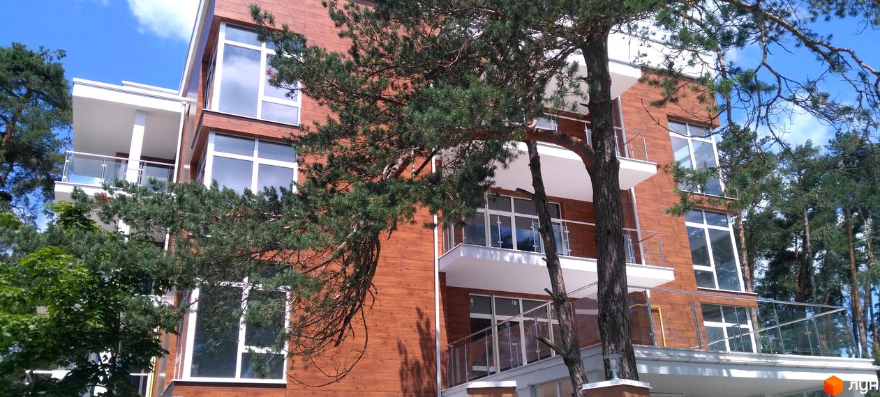 Зовнішній вигляд новобудови ЖК Грінвуд з дерев'яним фасадом та скляними балконами. Навколо будівлі ростуть зелені дерева.