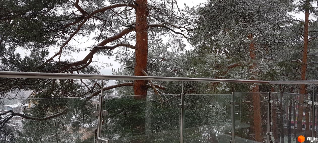 Вид на житловий комплекс Грінвуд із засніженими деревами. Сучасна новобудова з скляним балконом на тлі зимового пейзажу.