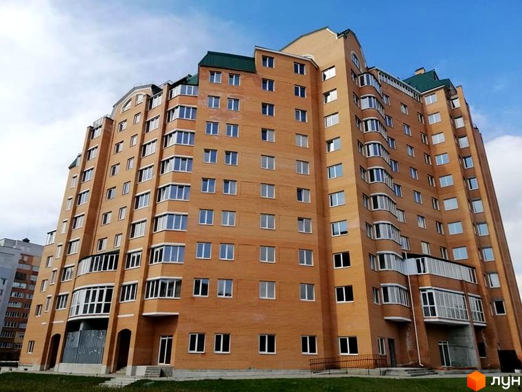 Висотна будівля ЖК Набережний з цегляним фасадом та великою кількістю вікон. На прибудинковій території є зелена трава.