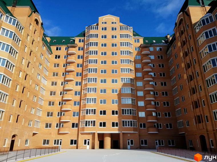 Висотна будівля ЖК Набережний з великою кількістю вікон та балконами. Простора прибудинкова територія з парковкою.