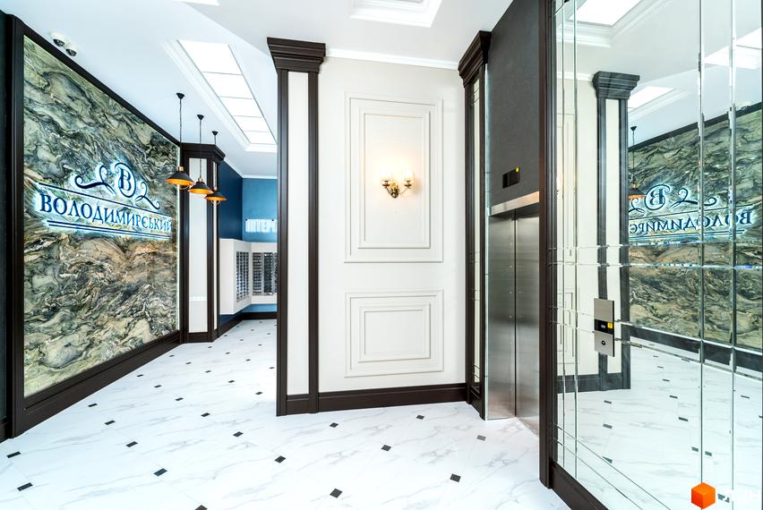 Інтер'єр холу ЖК Володимирський з мармуровими стінами, дзеркалами та ліфтом. Просторий хол з білою плиткою на підлозі та декоративним освітленням.
