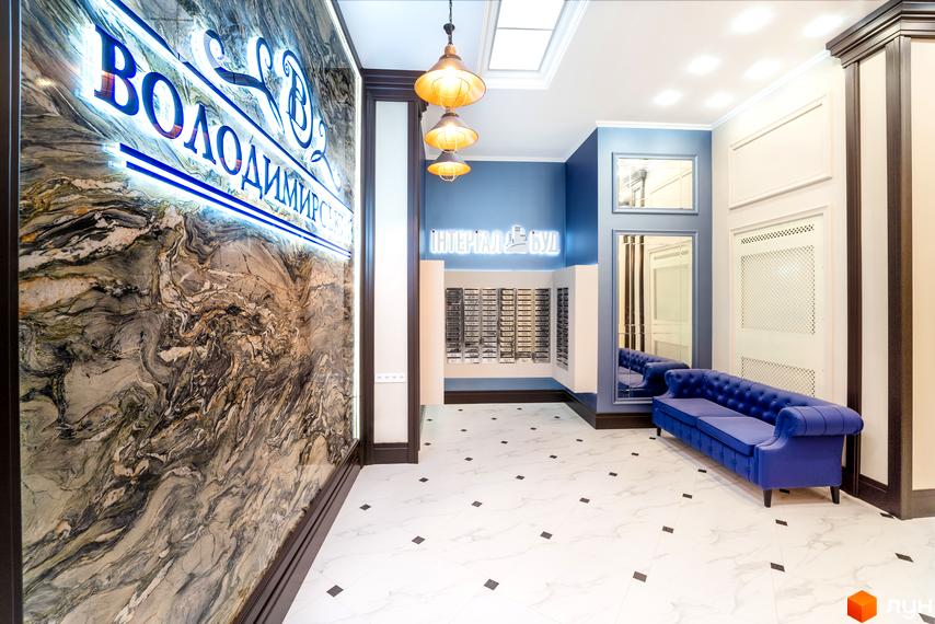 Розкішний хол ЖК Володимирський з мармуровою стіною та елегантним диваном. Просторий інтер'єр з яскравим освітленням та дизайнерськими деталями.