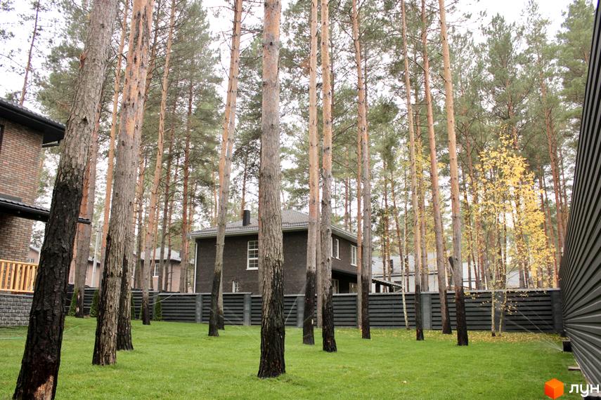 Котеджне містечко Квітка Полонини. Цегляний будинок з темним дахом, навколо якого ростуть високі дерева та зелена трава.