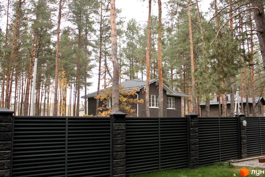 Будинок з темної цегли за чорним парканом на тлі соснового лісу. Котеджне містечко Квітка Полонини.