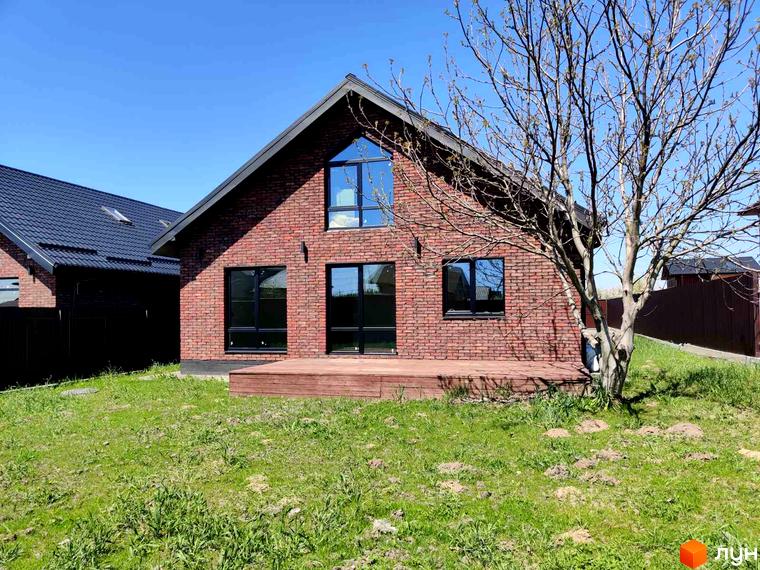 Котеджне містечко Одноповерховий Київ - Мархалівка. Цегляний будинок з великими вікнами та дерев'яною терасою на тлі зеленої галявини та блакитного неба.