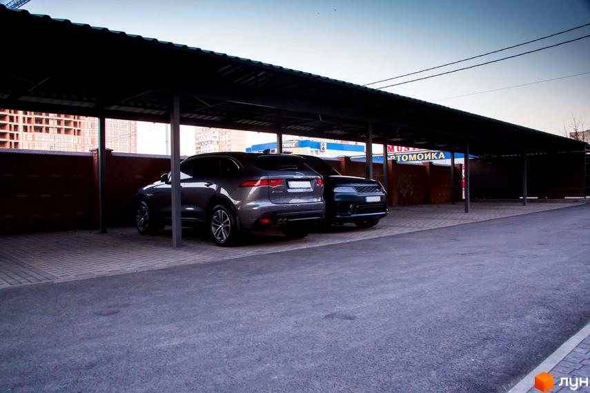 Сірий позашляховик стоїть під навісом біля цегляної стіни. На задньому плані видно будівництво житлового комплексу.