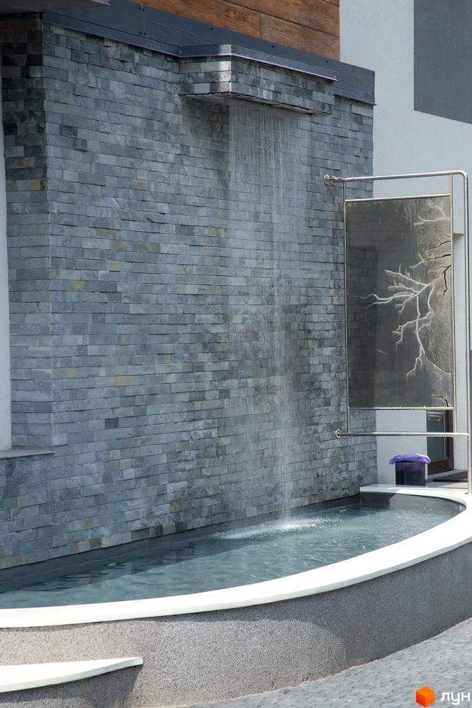 Водоспад у Житловому комплексі Cофія. Вигляд на стіну з сірої цегли та басейн з водою на території новобудови.