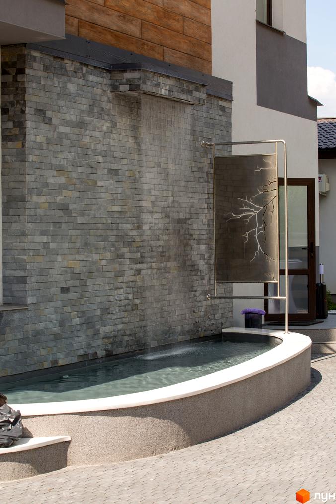 Житловий комплекс Cофія з фасадом з сірої цегли та декоративним водоспадом. На передньому плані басейн з водою.