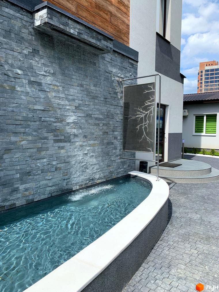 Фасад будинку з сірого каменю з водоспадом та басейном. На прибудинковій території бруківка та декоративна рослинність. ЖК Софія.