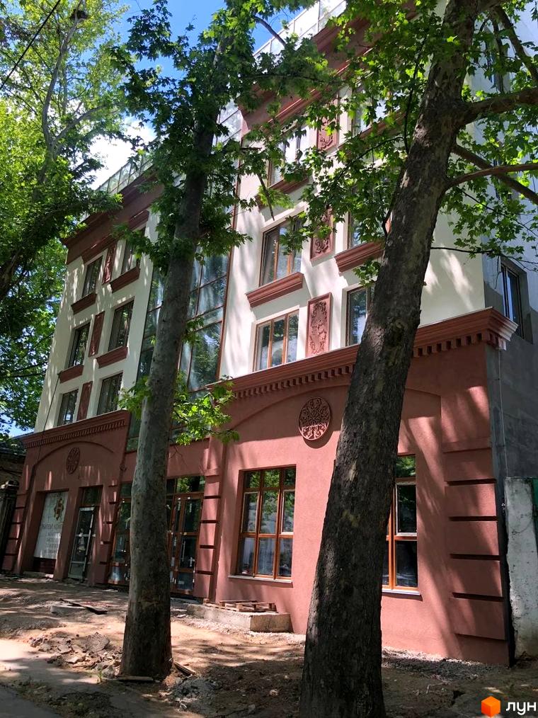 Зовнішній вигляд будівлі Житловий комплекс L7 House з фасадом у світлих тонах, обрамлений деревами. На першому поверсі розташовані вітрини.