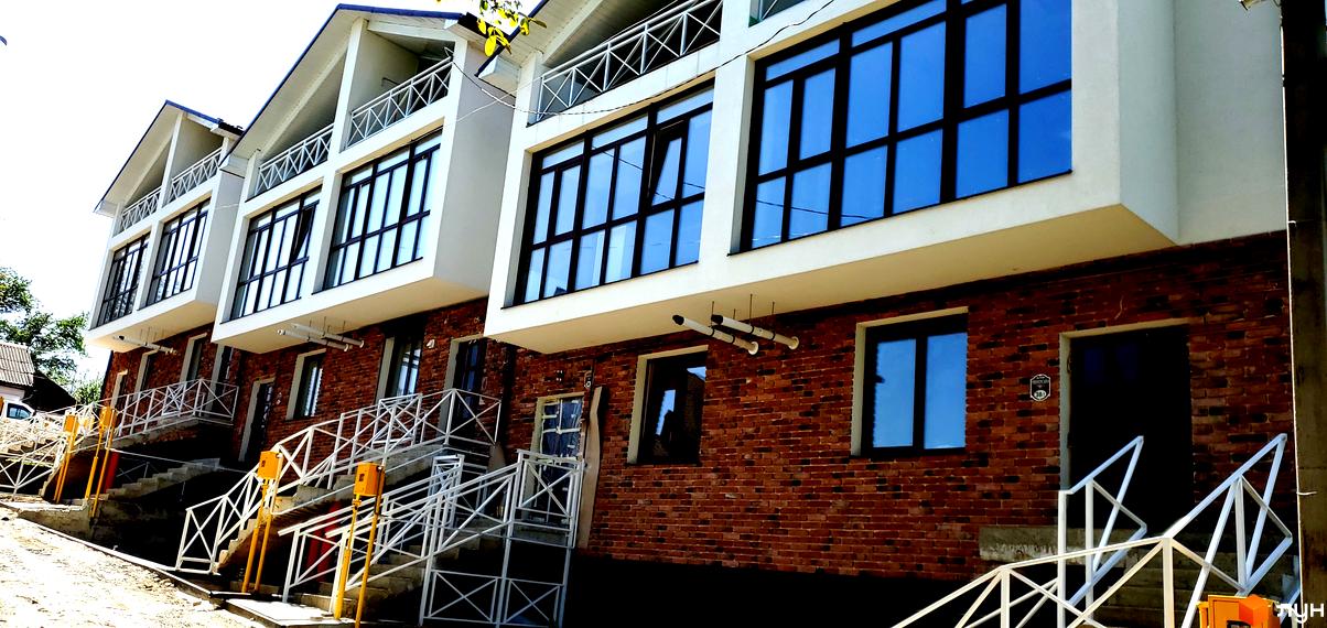Таунхауси Garden House на Рівненській: фасади з цегляною кладкою та великими вікнами, сходи з білими поручнями та жовтими опорами.