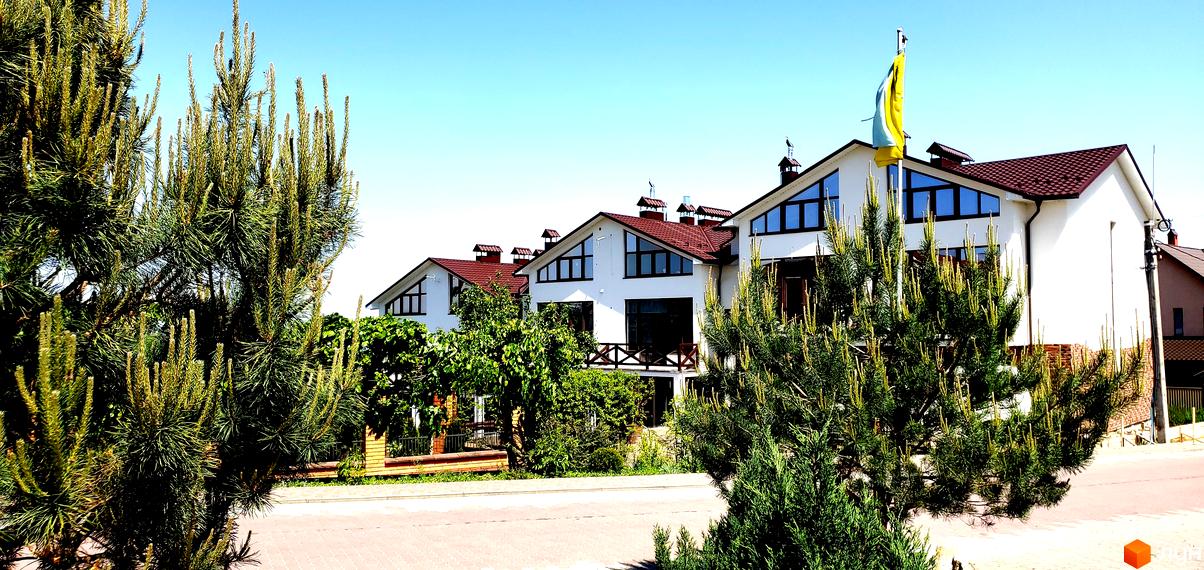 Таунхауси „Гарден Хаус“ на Рівненській: білі будинки з коричневими дахами та великими вікнами. Територія озеленена деревами та кущами, є бруківка.