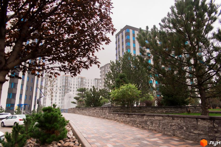 Житловий комплекс У-Квартал. Сучасні багатоповерхові будинки з блакитними вікнами та доглянута прибудинкова територія з пішохідною доріжкою та зеленими насадженнями.