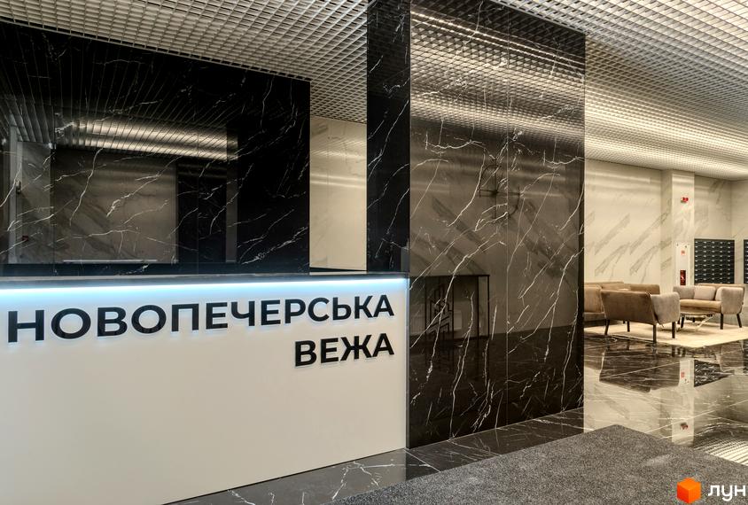 Інтер'єр холу Новобудови Новопечерська Вежа з мармуровими стінами та стійкою рецепції. Вигляд зони відпочинку з м'якими меблями.