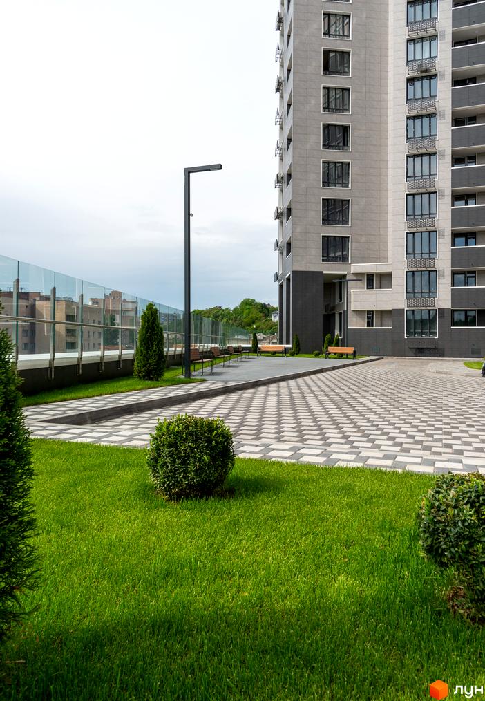 Зовнішній вигляд багатоповерхового будинку в Житловому комплексі Новопечерська Вежа. На передньому плані зелений газон та доріжка з тротуарної плитки.