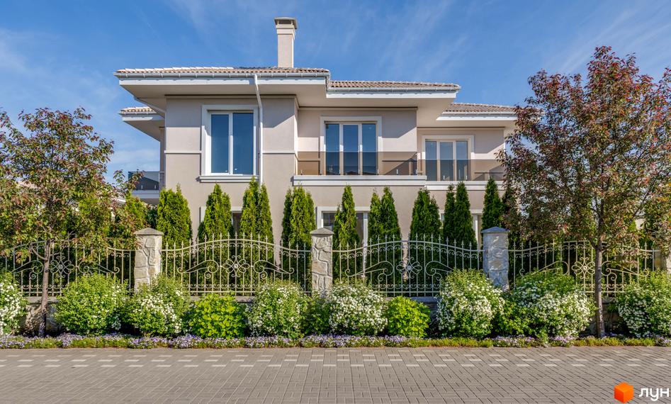 Двоповерховий будинок з великими вікнами та балконом, перед будинком кований паркан та зелені насадження. КМ Золоче Прованс - ідеальне місце для життя.